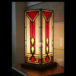 Peut inclure: Une lampe de table en verre coloré avec un motif géométrique en rouge, jaune et blanc. La lampe a une base en bois.