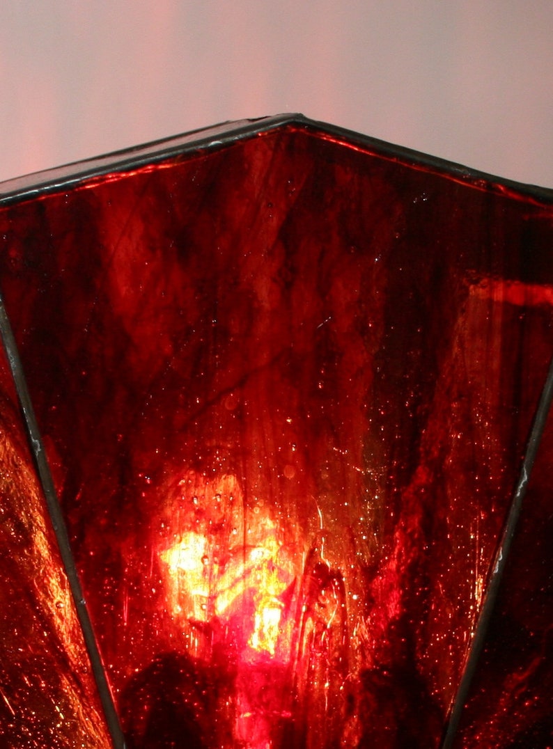 Op de afbeelding: Een rode lampenkap van glas-in-lood met een licht dat erdoorheen schijnt.