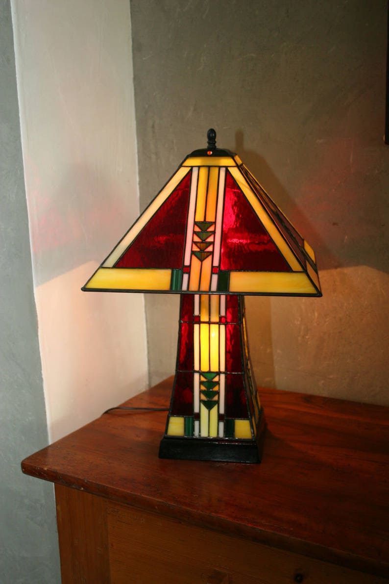May include: A stained glass table lamp with a red, yellow, and green geometric design. The lamp is on a wooden table.
