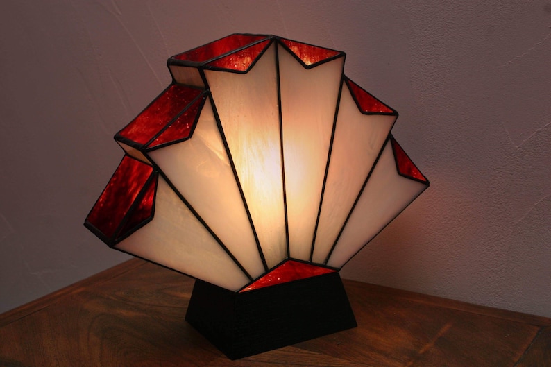 Op de afbeelding: Een rood-witte Tiffany-lamp met een geometrisch ontwerp. De lamp staat op een houten tafel.