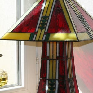 May include: A stained glass lamp with a red, yellow, and green geometric design. The lamp has a wide base and a tall, slender shade.