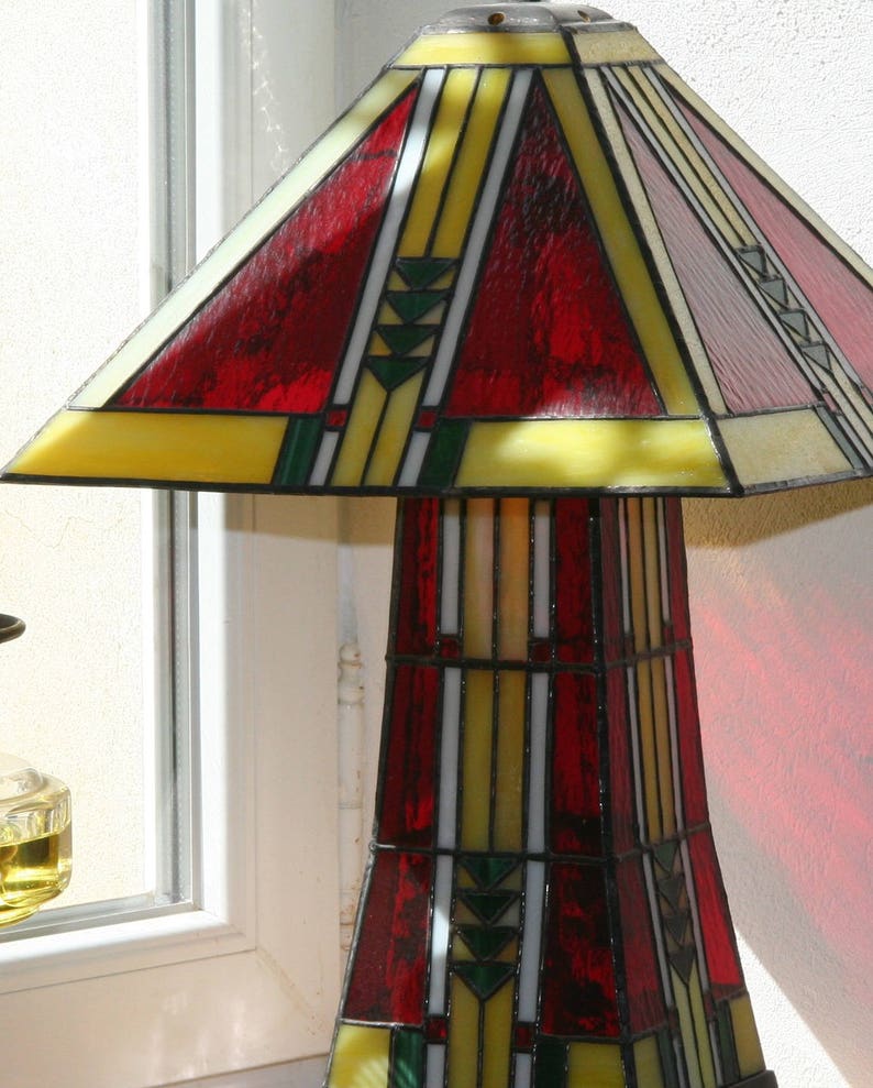 May include: A stained glass lamp with a red, yellow, and green geometric design. The lamp has a wide base and a tall, slender shade.