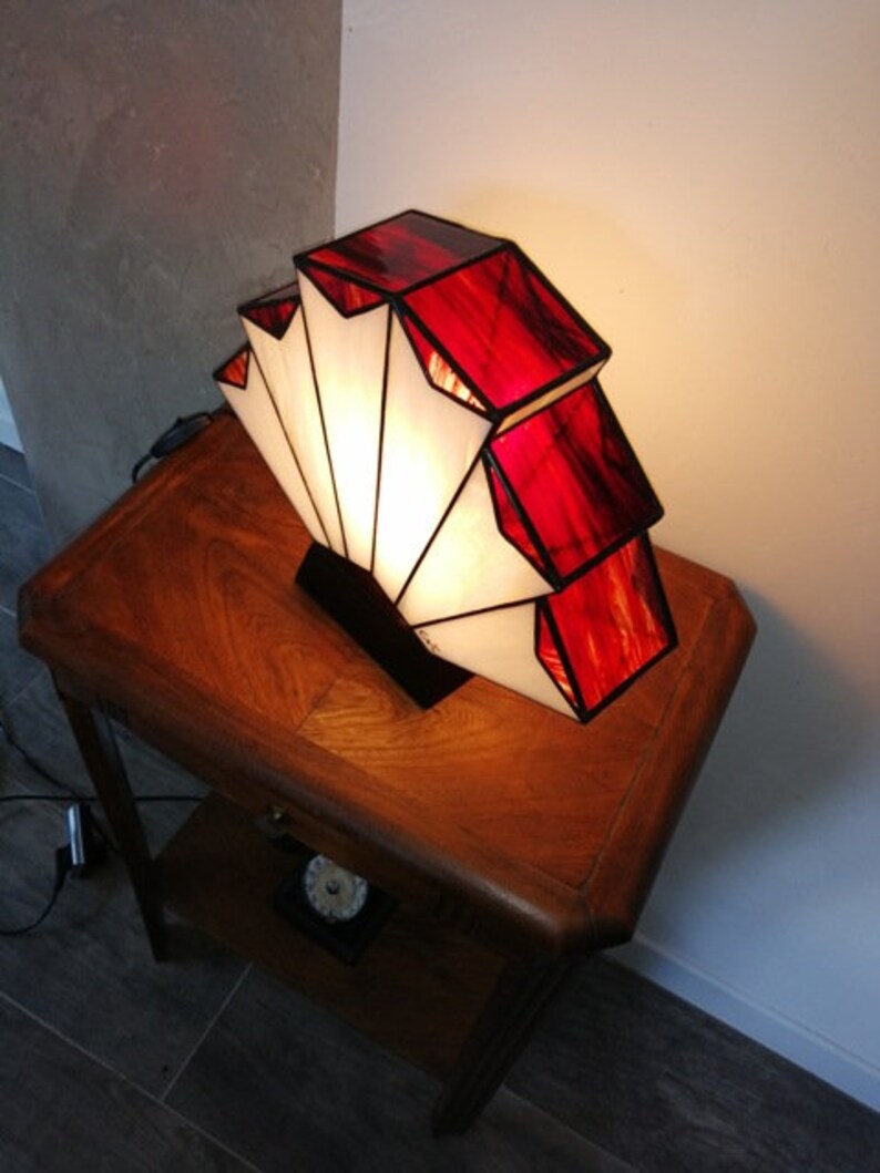 Op de afbeelding: Een rood-witte Tiffany-lamp in de vorm van een waaier. De lamp staat op een houten tafel.