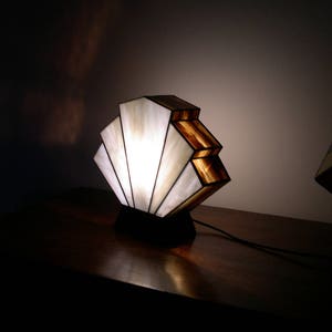 May include: A white and brown stained glass lamp with a fan-shaped design. The lamp is on a dark wooden surface and is lit.