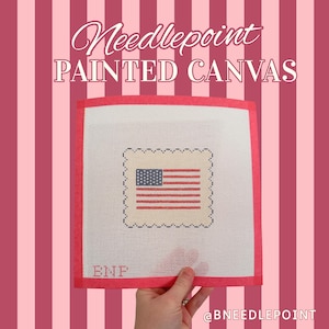 May include: Needlepoint painted canvas featuring an American flag design. The canvas has a red border and the text "Needlepoint PAINTED CANVAS" is displayed at the top. The canvas is held by a hand.