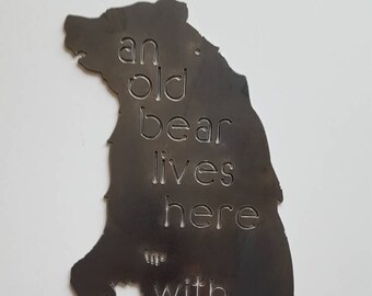 May include: A metal silhouette of a bear with the text "an old bear lives here with his honey" etched into the metal.