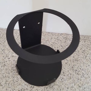 May include: Black metal can holder with a circular opening and a flat base. The holder is designed to be mounted on a wall.