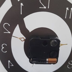 May include: A black and white clock with a bicycle design. The clock face is a circle with Roman numeral markings. The clock hands are gold and the clock mechanism is visible in the center.