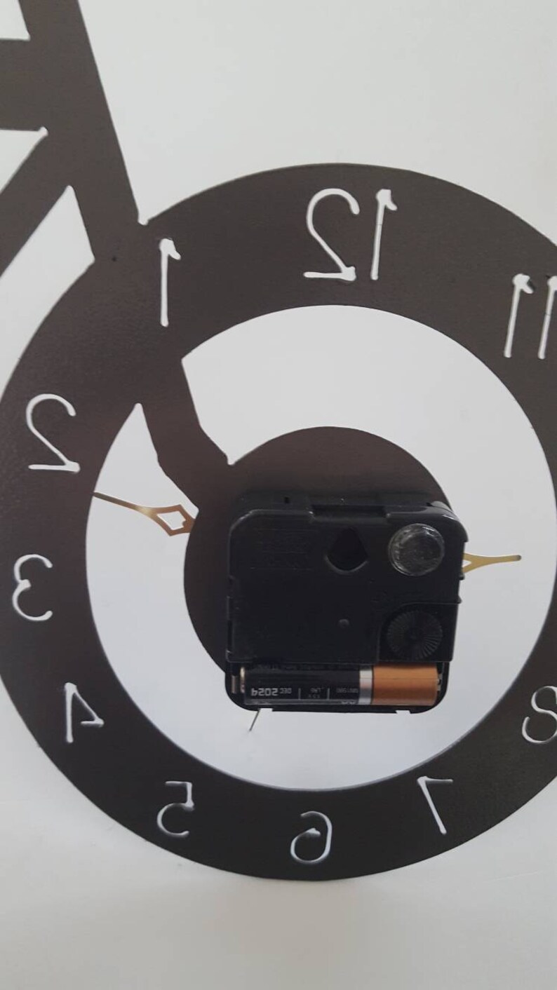 May include: A black and white clock with a bicycle design. The clock face is a circle with Roman numeral markings. The clock hands are gold and the clock mechanism is visible in the center.