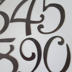 May include: A set of black metal house numbers, including the numbers 3, 4, 5, 8, 9, and 0. The numbers are in a decorative, cursive font.
