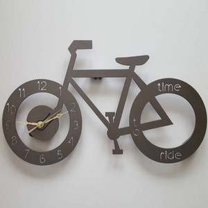 May include: A brown metal wall clock shaped like a bicycle with the words "time to ride" on the back wheel.