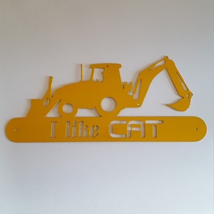 May include: Yellow metal wall art featuring a silhouette of a Caterpillar excavator with the text "I like CAT" below.