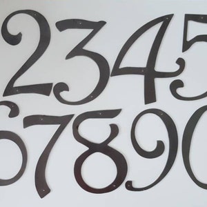 May include: A set of ten black metal house numbers, each with a unique, stylized design. The numbers are 1, 2, 3, 4, 5, 6, 7, 8, 9, and 0.
