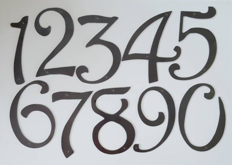 May include: A set of ten black metal house numbers, each with a unique, stylized design. The numbers are 1, 2, 3, 4, 5, 6, 7, 8, 9, and 0.
