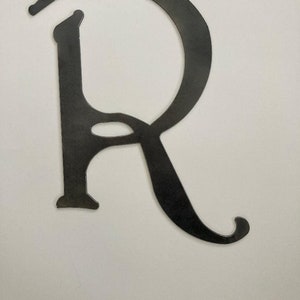 May include: A metal letter R with a decorative, cursive font. The letter is black and has a hole at the top for hanging.