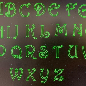 May include: A green alphabet with a decorative, cursive font. Each letter is outlined in green and has a black background.
