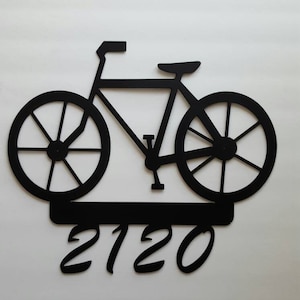May include: Black metal silhouette of a bicycle with the number 2120 below it.