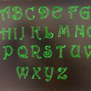 May include: A green alphabet with decorative lettering on a black background.