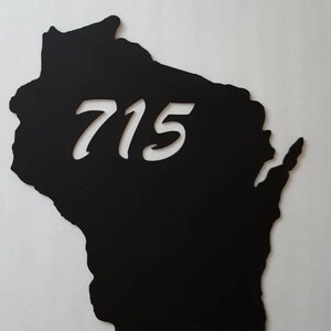Puede incluir: Silueta negra del estado de Wisconsin con el número 715 recortado en blanco.