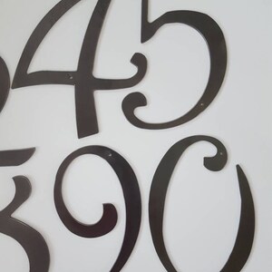 May include: A set of black metal house numbers in a decorative script font. The numbers are 4, 5, 3, 9, and 0.