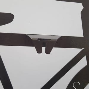 May include: Black metal silhouette of a bicycle with a clock face on the front wheel. The clock face has Roman numerals and a silver hand.