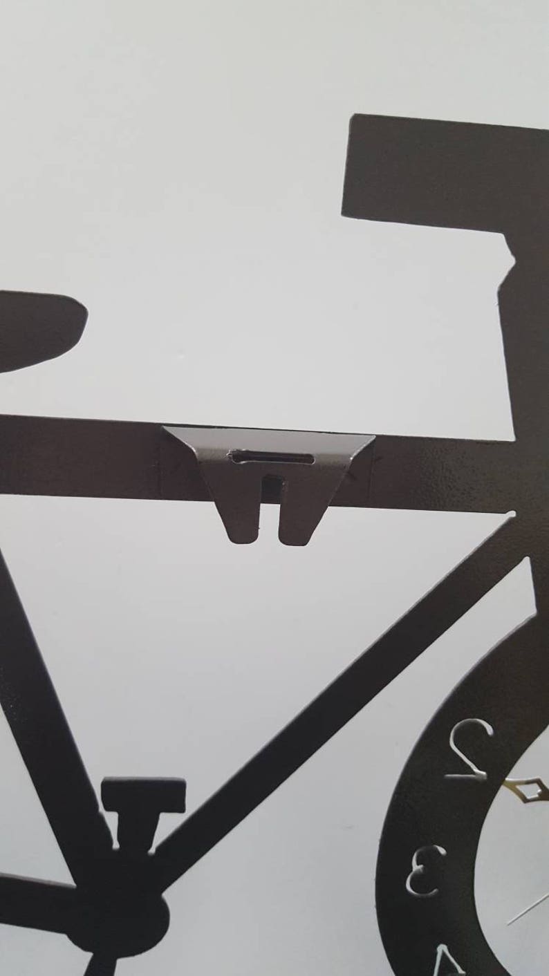 May include: Black metal silhouette of a bicycle with a clock face on the front wheel. The clock face has Roman numerals and a silver hand.