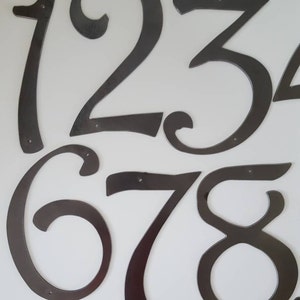 May include: A set of black metal house numbers, 1, 2, 3, 6, 7, and 8, with a decorative, cursive font. The numbers are individually cut and have a slightly distressed finish.