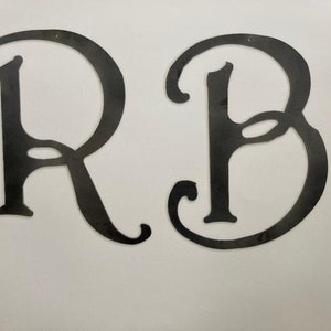 May include: Two black metal letters, R and B, in a decorative script font.