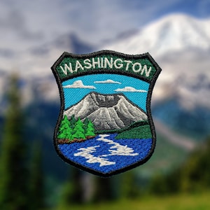 Peut inclure: Un écusson brodé en forme de bouclier portant le mot WASHINGTON en lettres blanches sur le haut. Le motif représente un sommet de montagne gris, des pins verts et une rivière bleue coulant dans un paysage sous un ciel bleu clair nuageux.