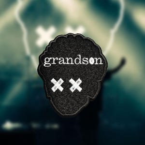 Op de afbeelding: Zwarte geborduurde patch met het woord "grandson" in witte tekst en twee witte "X" symbolen.