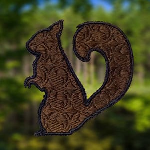 Peut inclure: Une applique en tissu marron en forme d'écureuil avec un motif détaillé. L'écureuil est tourné vers la gauche et sa queue est enroulée autour de son corps.