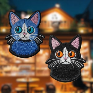 May include: Two embroidered cat patches. One is blue with white markings and the other is black with white markings. Both have orange eyes.