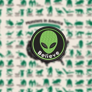 May include: Embroidered patch featuring a green alien head with black eyes on a black background, surrounded by a green border. The word "Believe" is embroidered in white. The background includes silhouettes of various monsters and the text "Monsters in America."