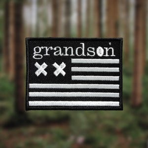 Könnte beinhalten: Schwarz-weiß gestickter Patch mit dem Text "grandson" und zwei weißen "X" über fünf weißen Streifen auf schwarzem Hintergrund.