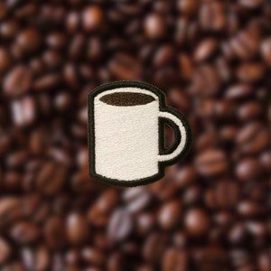 Op de afbeelding: Een witte koffiemok met een zwarte omtrek en een bruine koffie vulling. De mok is op een achtergrond van koffiebonen.