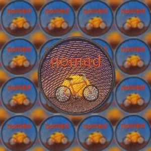 Puede incluir: Un primer plano de un parche redondo bordado con una escena de puesta de sol y una bicicleta. El parche es marrón con acentos naranja, amarillo y blanco. El texto "Nomad" está bordado en rojo en el parche.