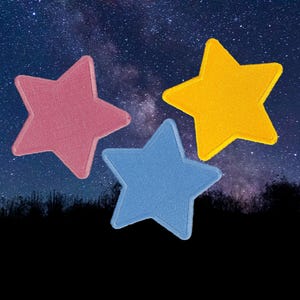 May include: Three star-shaped patches in pink, blue, and yellow. The patches are against a backdrop of a starry night sky and a dark silhouette of a landscape.