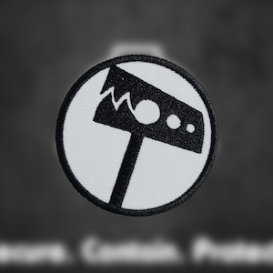 May include: A white circular patch with a black embroidered image of a hammer with a jagged edge. The hammer has a round head with two small circles.