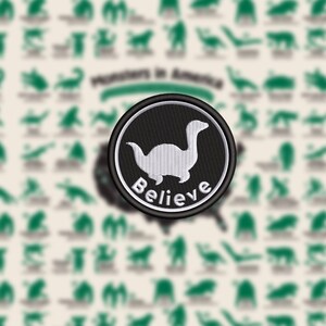 May include: Embroidered patch featuring a white dinosaur-like creature on a black background, encircled by a white border. The word "Believe" is arched below the creature. The background includes silhouettes of various creatures and the text "Monsters in America".