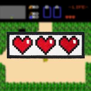 May include: A white patch with three red pixelated hearts, surrounded by a black border. The patch is a common video game health indicator.
