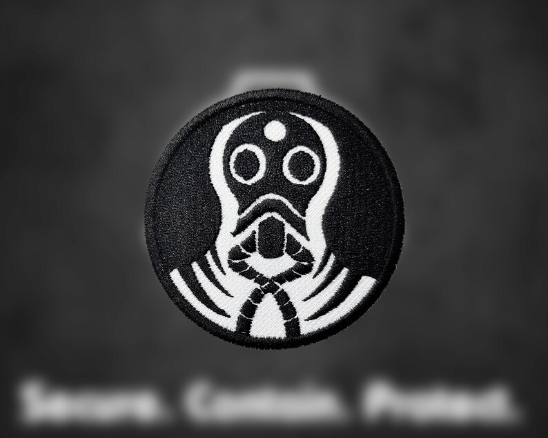May include: Black and white embroidered patch of a stylized gas mask with a single eye hole and a rope-like design around the neck.