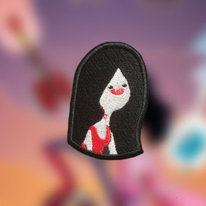 May include: Black and red embroidered patch of a cartoon woman with long black hair and a red dress.