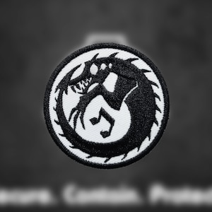May include: Black and white embroidered patch featuring a stylized creature with sharp teeth and claws. The creature is curled in a circle with its tail in its mouth.