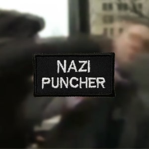 May include: Black and white embroidered patch with the text "NAZI PUNCHER" in white lettering.