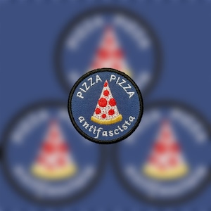 Puede incluir: Un parche redondo azul bordado con texto blanco que dice "Pizza Pizza Antifa-scista" y una rebanada de pizza roja y blanca con una corteza amarilla.