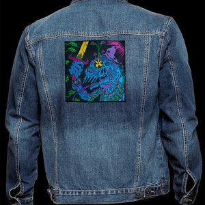 Pode incluir: Uma jaqueta de ganga azul com um remendo bordado colorido nas costas. O remendo apresenta um esqueleto com uma espada e uma coroa, rodeado de flores e videiras.