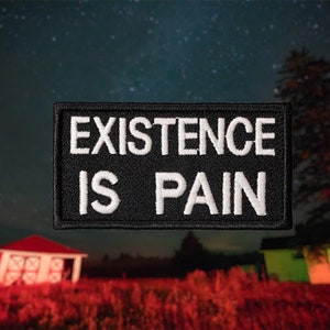 Puede incluir: Parche bordado en blanco y negro con el texto "EXISTENCE IS PAIN" sobre un fondo de cielo nocturno estrellado.