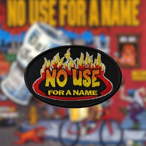 Peut inclure: Patch ovale noir et rouge avec les mots "NO USE FOR A NAME" en lettres jaunes et orange avec des flammes derrière le texte.