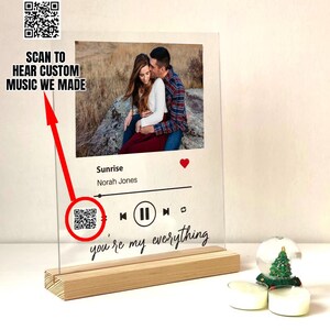以下が含まれることがあります： カップルの写真、曲の詳細、そして「you're my everything」というテキストが書かれた透明なアクリル板。木製のベースに取り付けられています。「SCAN TO HEAR CUSTOM MUSIC WE MADE」というテキストも表示されています。