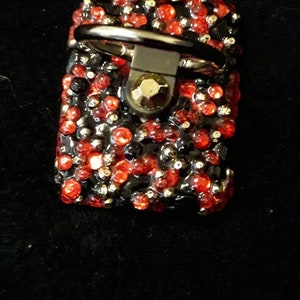 May include: A black phone ring holder with a silver ring and red and black rhinestones.